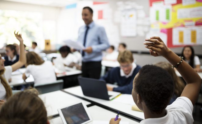 Students with their hands up responding to their teacher Students with their hands up responding to their teacher
