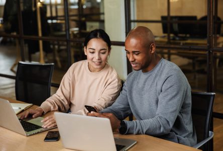 Image of multiethnic young female and male coworkers sitting at table and working on laptops in office